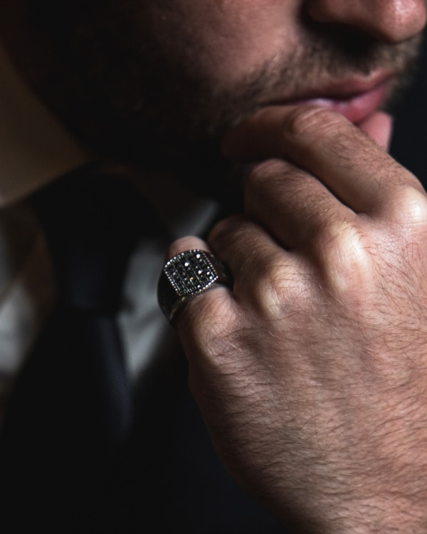 Hombre con barba apoyando el puño en su rostro, luce anillo Mosaico de acero quirúrgico Valurys con diseño geométrico decorativo.