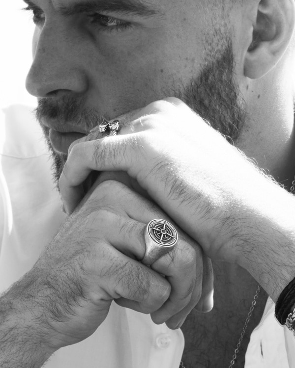 Hombre con barba, apoyando el rostro sobre las manos, luce anillo Valurys de acero quirúrgico con diseño de brújula y anillo de águila imperial.
