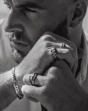 Hombre con barba luciendo la pulsera Enlazada y el anillo Ave Imperial de Valurys, ambos en acero quirúrgico, reflejando un estilo masculino y robusto.