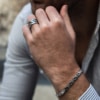 Hombre vistiendo camisa de rayas, con pulsera de eslabones de acero quirúrgico Valurys y anillos gruesos en la mano.