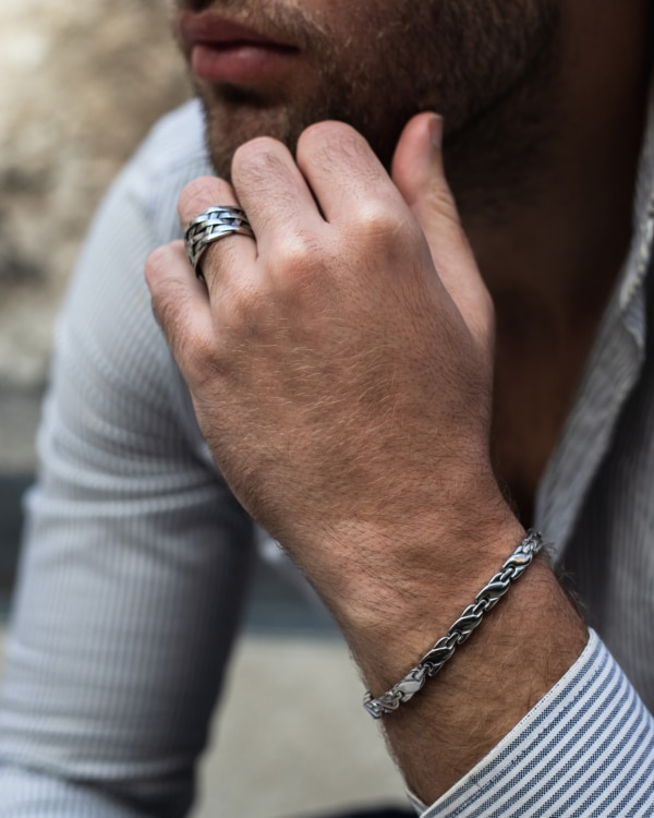 Hombre vistiendo camisa de rayas, con pulsera de eslabones de acero quirúrgico Valurys y anillos gruesos en la mano.