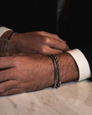 Muñeca masculina con dos pulseras de acero Valurys sobre mesa de mármol, una de eslabones y otra de cadena trenzada.